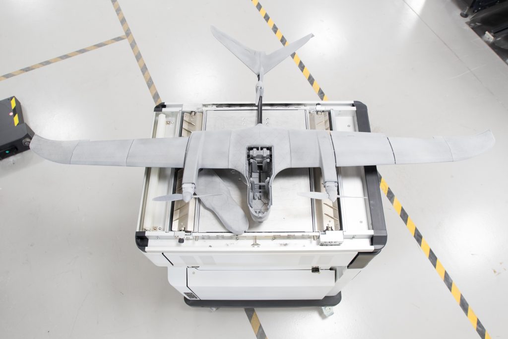 A 3D printed drone. The drone looks like a small plane with exposed propellors on both wings. It is sat on top of a metal box.