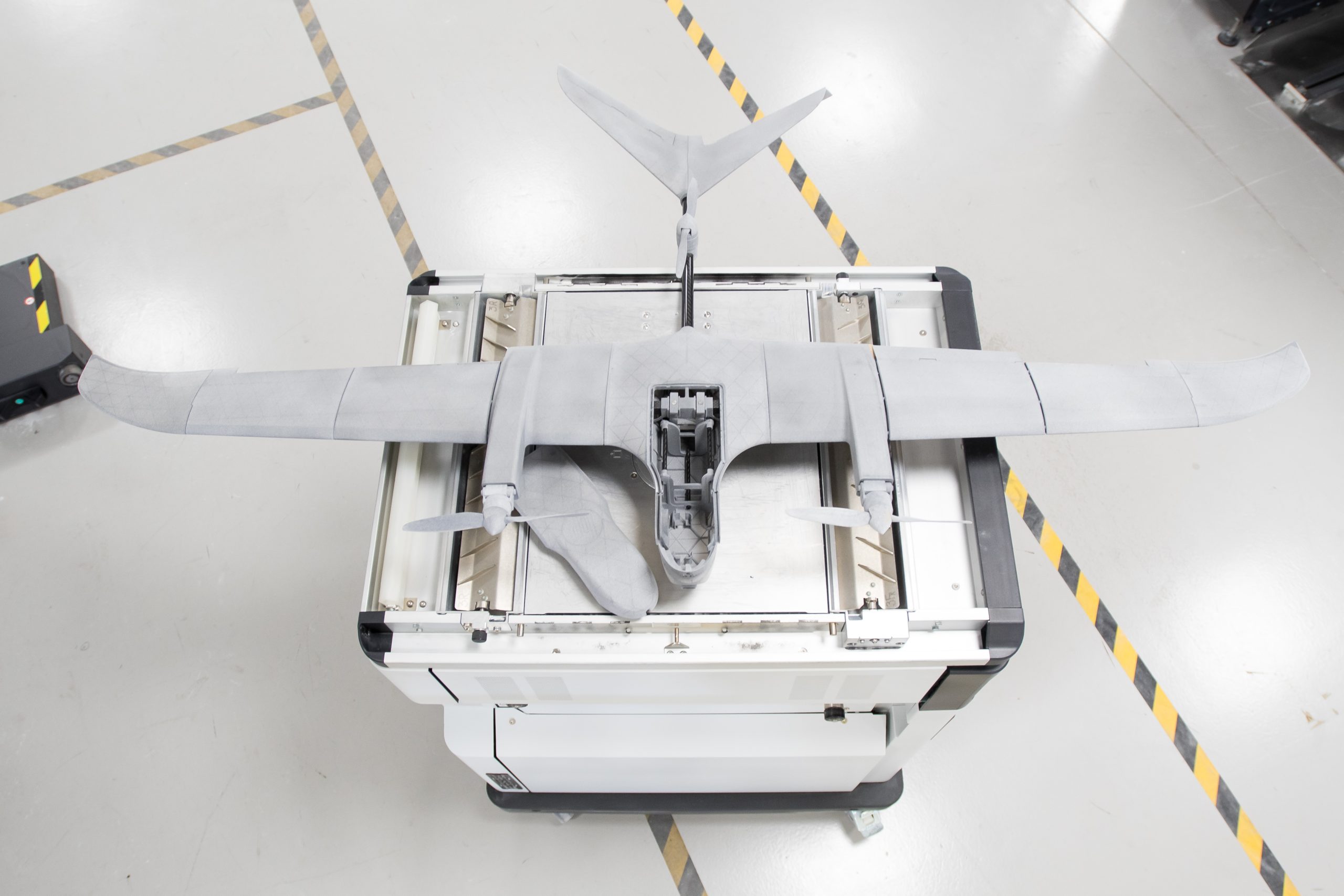 A 3D printed drone. The drone looks like a small plane with exposed propellors on both wings. It is sat on top of a metal box.