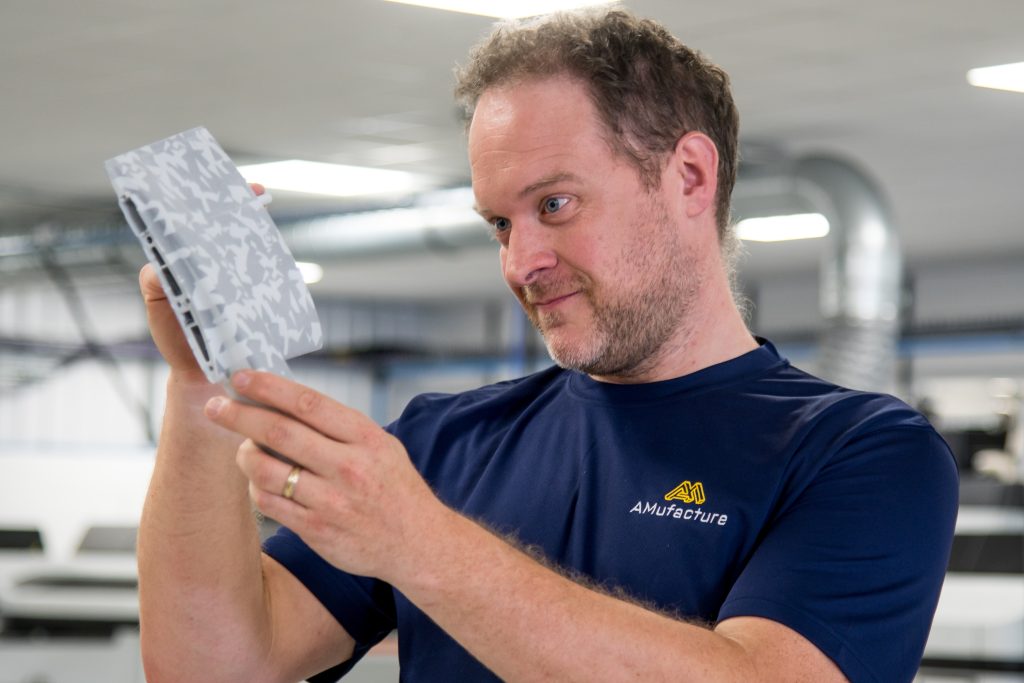 A person looking at a 3D printed component held in their hands. The component has a white camo print.
