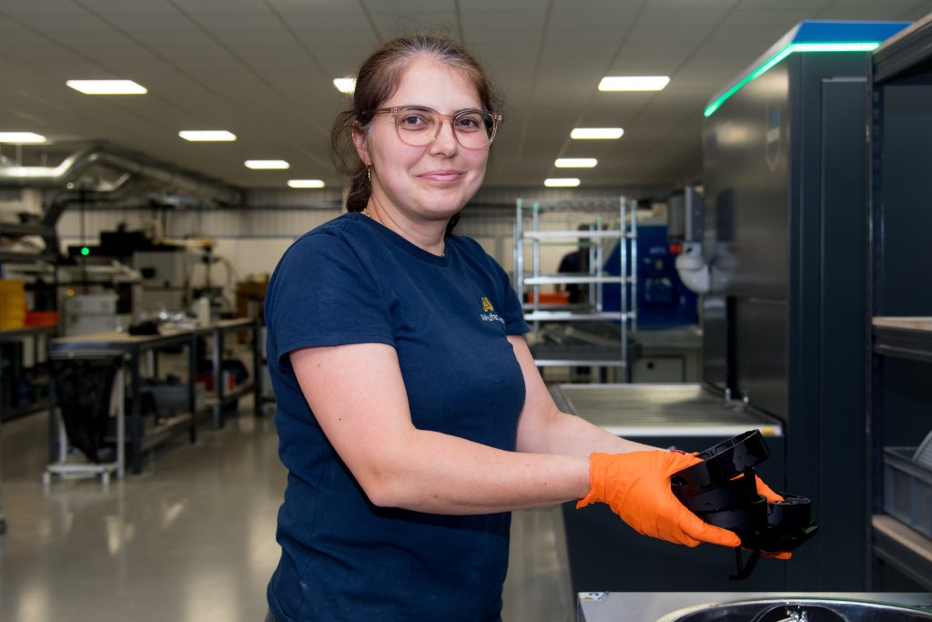 A person holding 3d printed parts, looking straight at the camera smiling.
